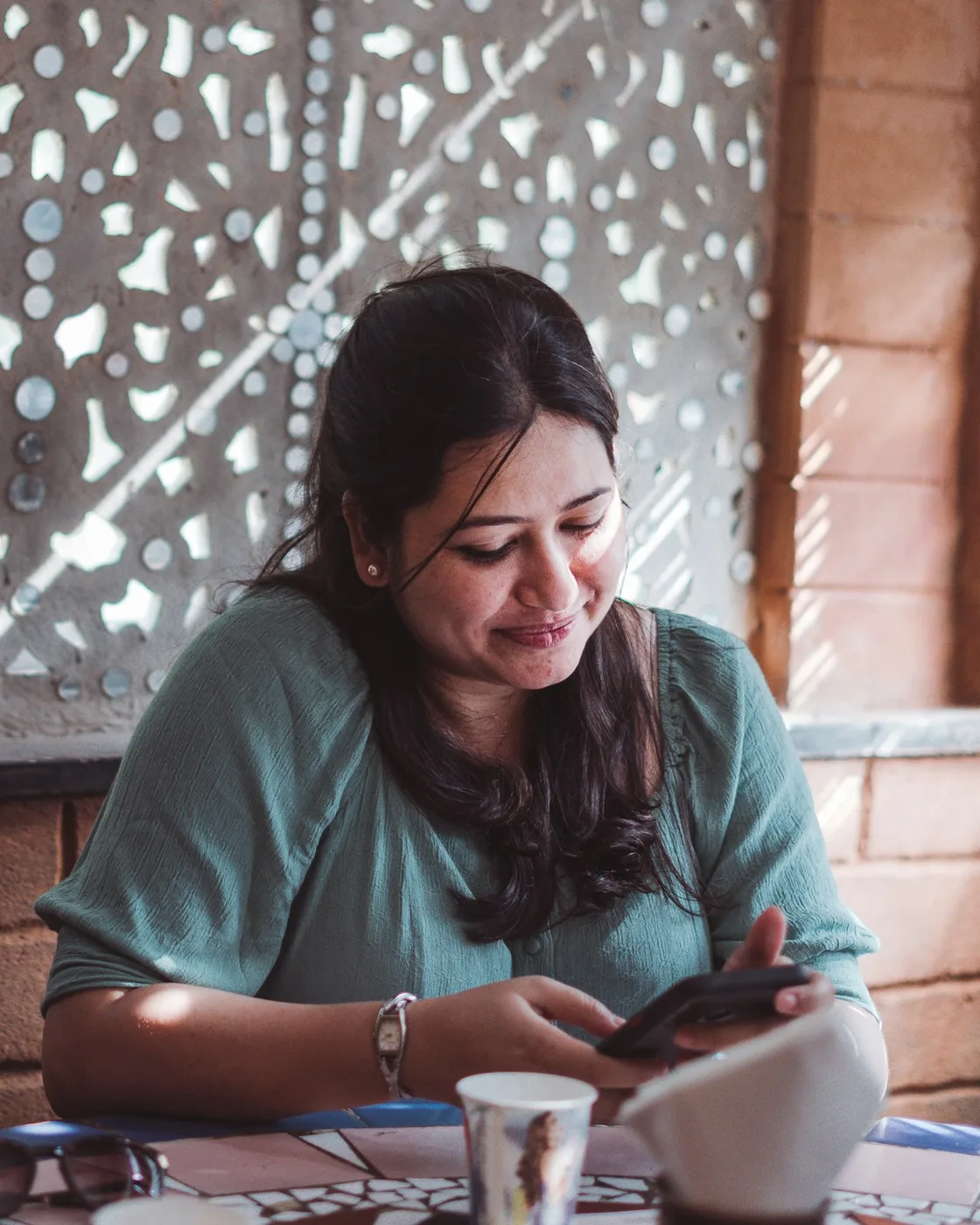 A woman smiling while reviewing her finances on her phone over coffee